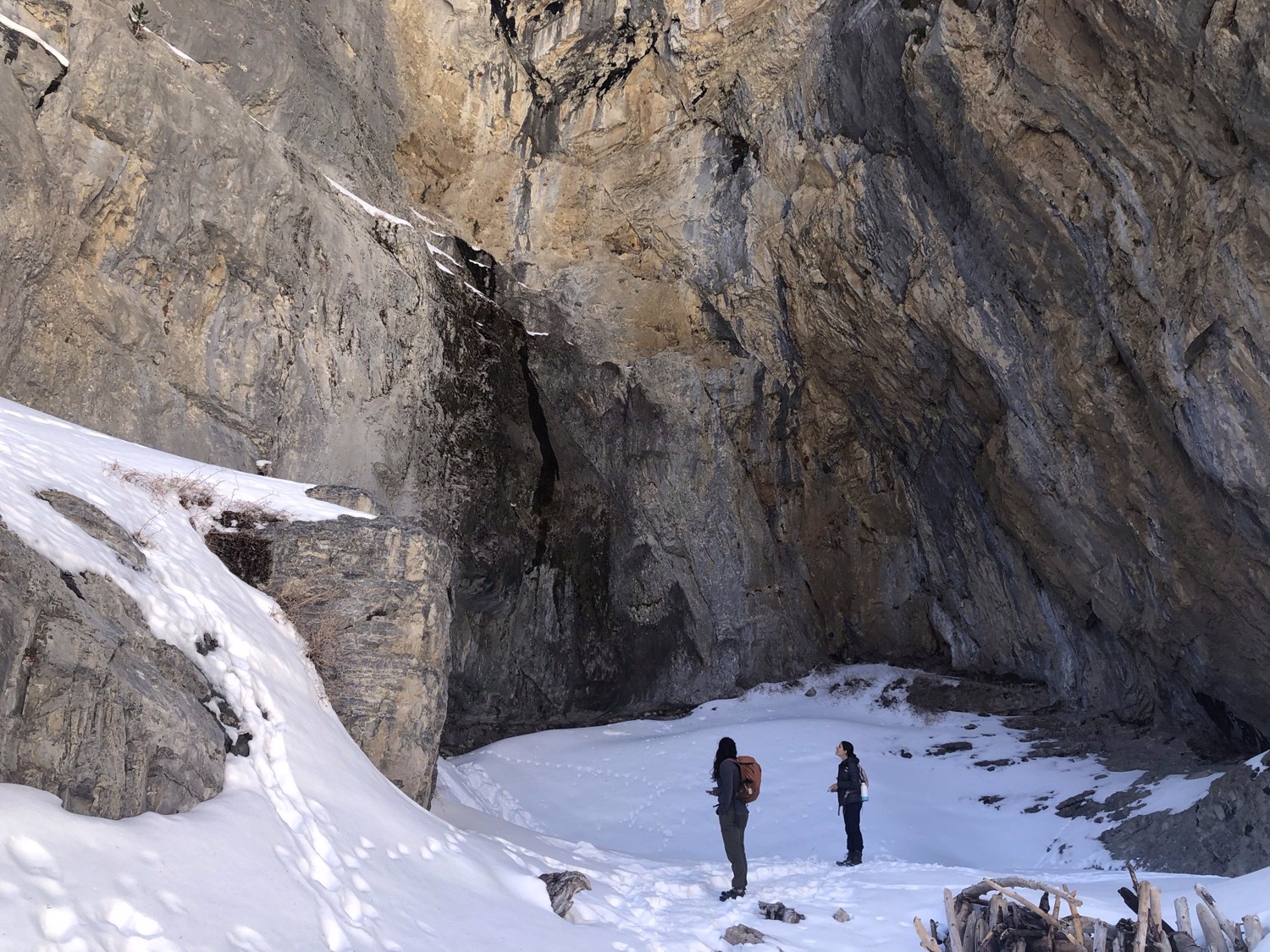 Two hikers cross a snow-covered canyon beneath tall gray walls.