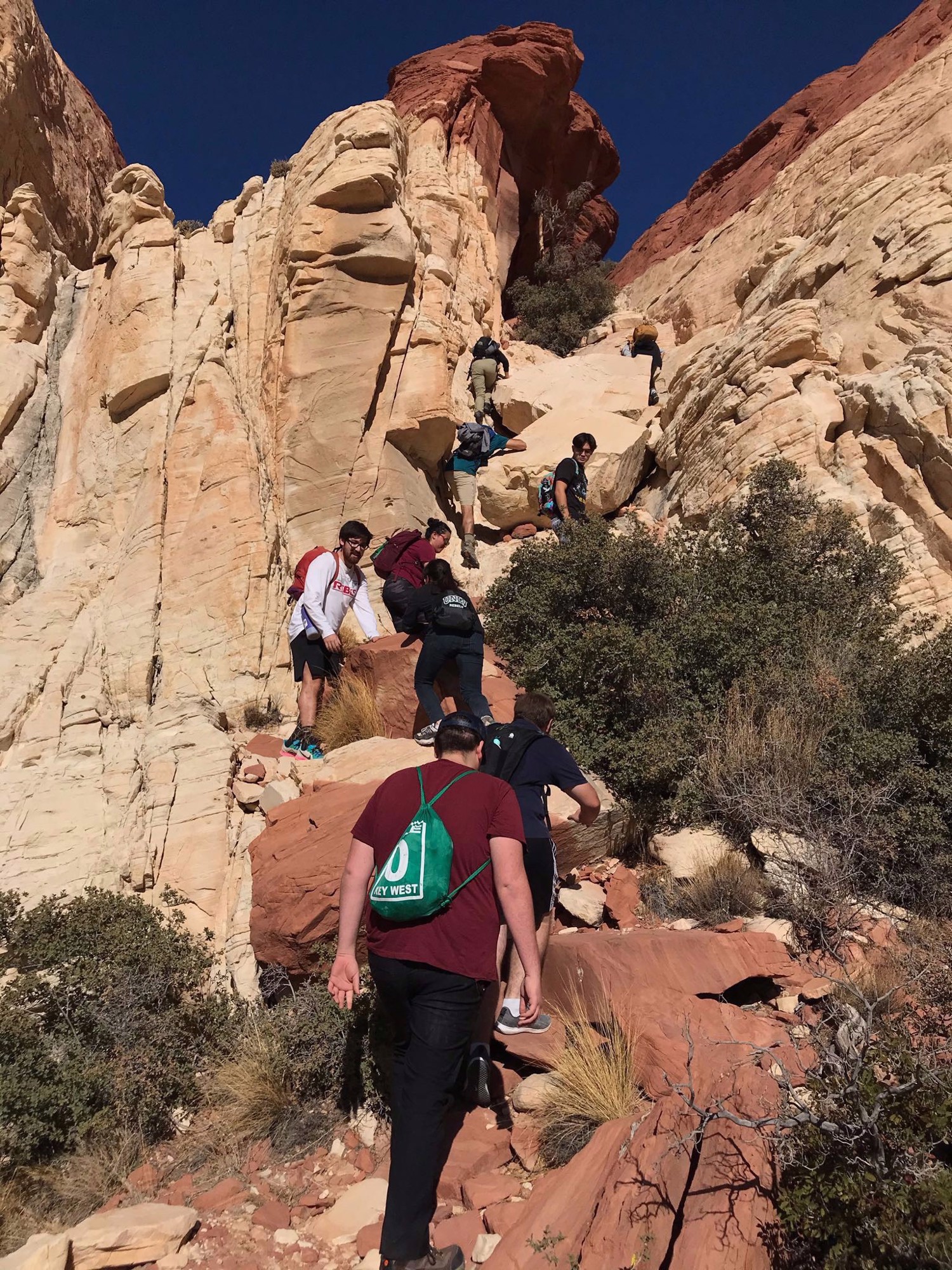 A group hikes single file through a steep sandstone passage.