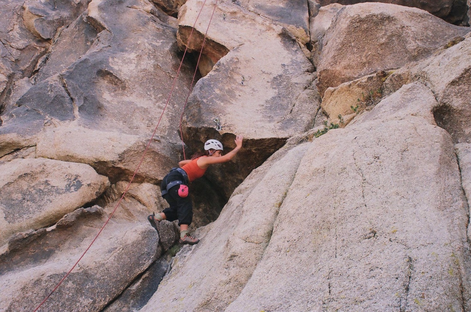A climber in red pants ascends a light-colored rock wall.