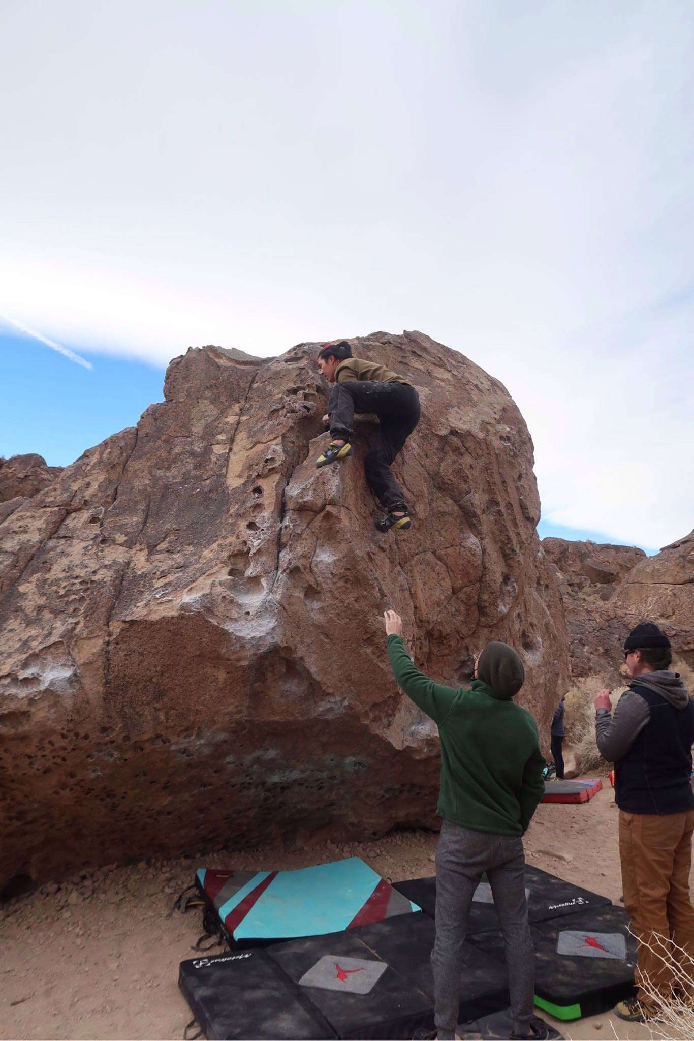 A climber works up a sandstone boulder while club members spot from below.