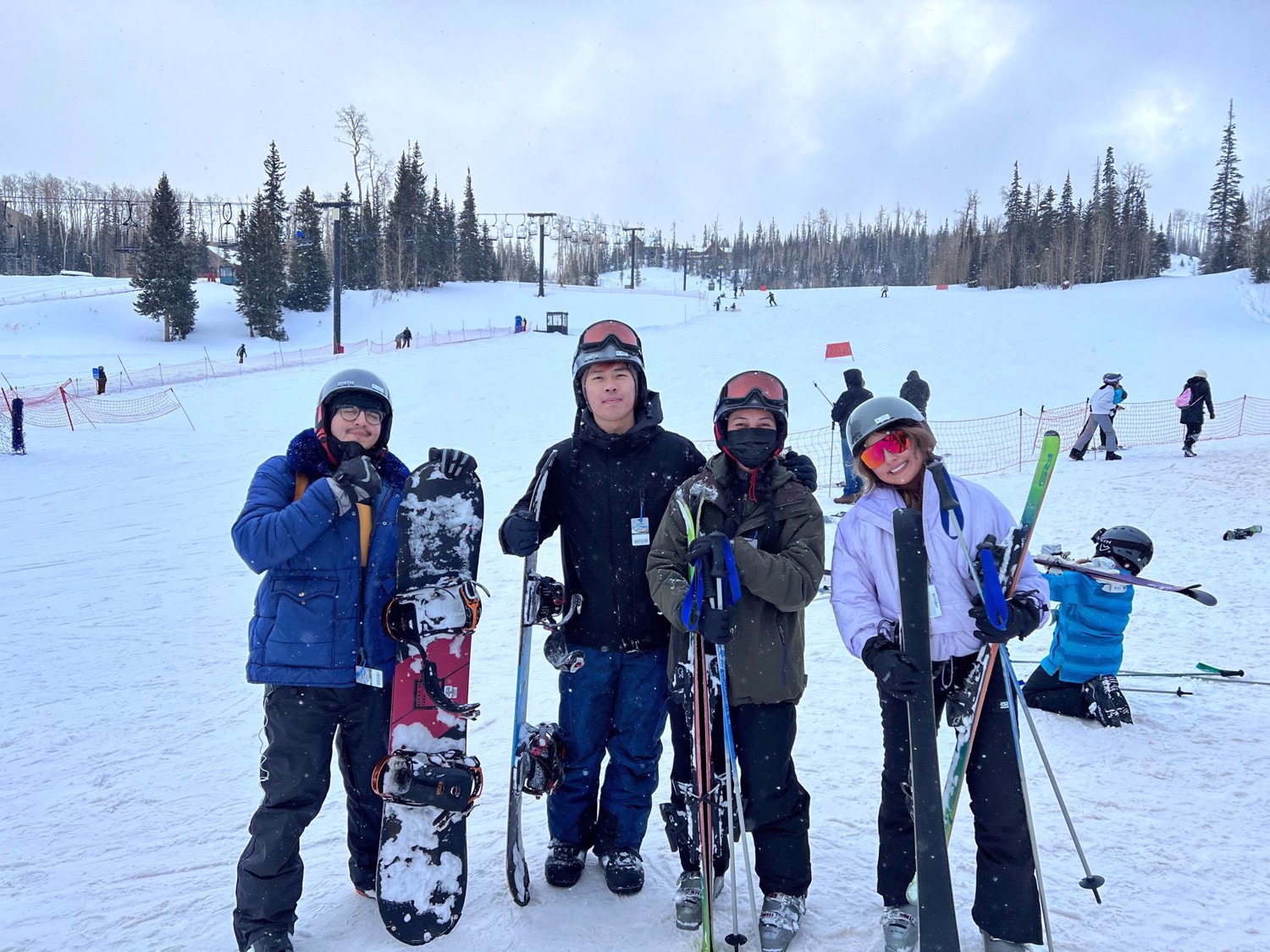 Four Mountain Club members pose together in the snow with skis and snowboards.