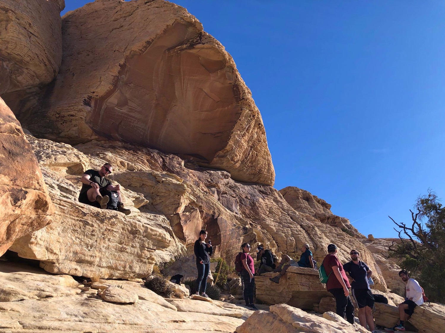 Club members rest on a sandstone ledge beneath a massive rounded boulder.