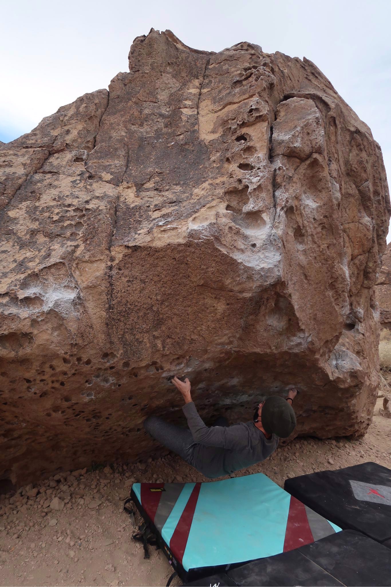 A Mountain Club member climbs a tan boulder with two spotters nearby.
